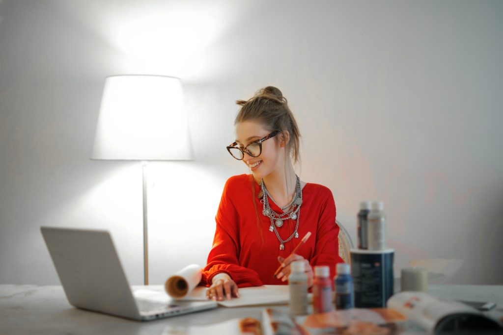 A young woman in a bright red blouse and glasses sits at her home office desk as she gets to work raising funds for a nonprofit organization.