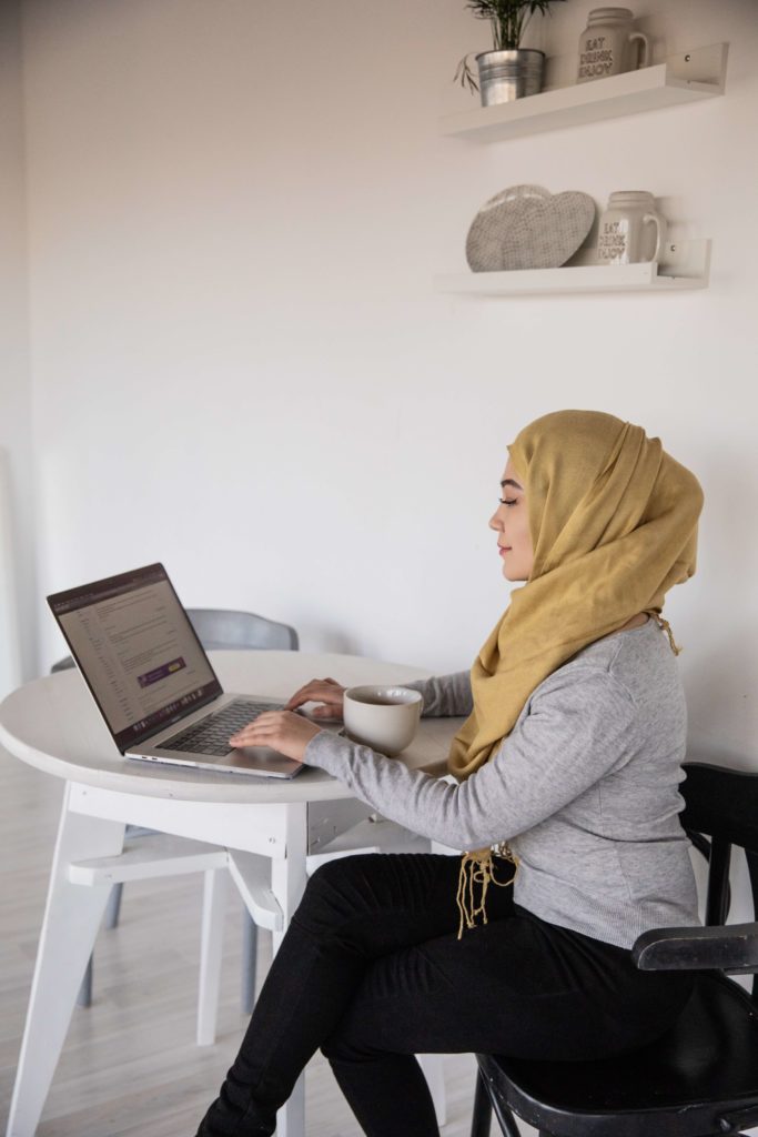 A young woman with a yellow hijab uses her computer to implement a sustainable fundraising strategy for a nonprofit