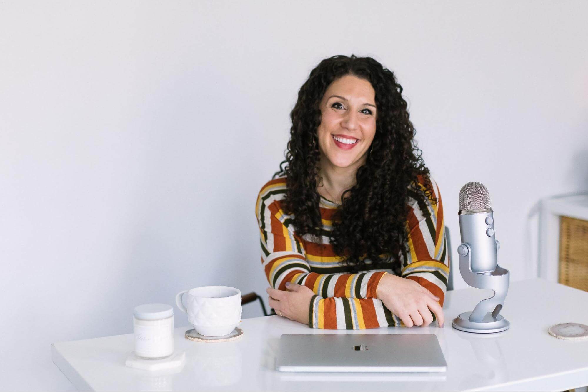 Mallory Erickson sits at a desk with her laptop, a coffee mug, and a podcast microphone.